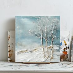 two paintings are sitting on a shelf next to each other, one is white and the other is blue