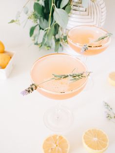 two glasses filled with lemonade sitting on top of a table next to sliced lemons