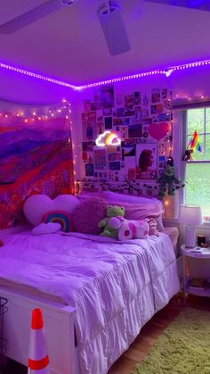 a bedroom decorated in purple and white with pictures on the wall, lights strung from above