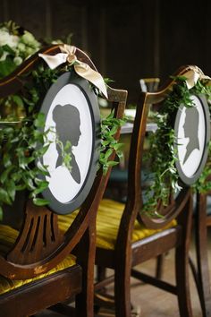 two wooden chairs decorated with greenery and silhouettes on them, sitting next to each other