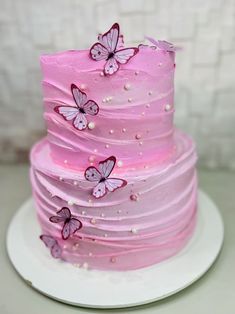 a three tiered cake with pink frosting and butterflies on it