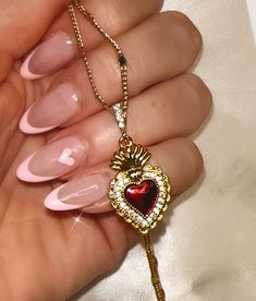 a woman's hand with pink manies and a heart shaped pendant on it