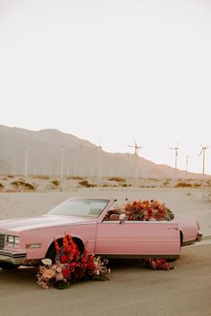 a pink car with flowers on the hood parked in front of wind mills and windmills