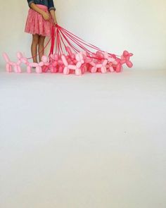 a woman in pink is pulling balloons on a white surface with a red string attached to it