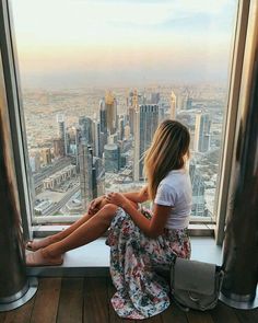 a woman sitting on top of a window sill looking out at the cityscape