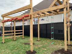 a wooden structure with swings and ladders on the grass in front of a house