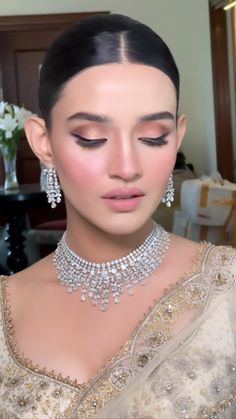 a woman wearing an elaborate necklace and earrings with her eyes closed, looking down at the camera