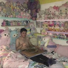 a shirtless man sitting in bed surrounded by stuffed animals and other stuff animals on shelves