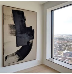 an abstract painting hangs on the wall next to a large window overlooking a cityscape