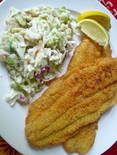 fish, coleslaw and lemon wedges on a white plate