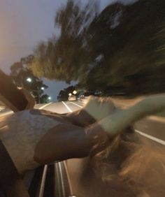 a person riding in the back of a car on a road at night with trees and street lights