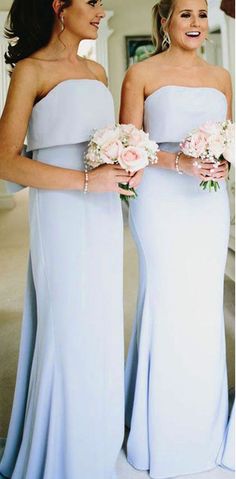 two bridesmaids in light blue dresses smile at each other while holding bouquets