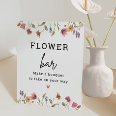 a white vase with flowers in it next to a sign that says flower bar make a bouquet to take on your way