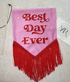 a pink and red banner with the words best day ever on it next to knitting needles