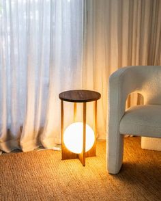 a white chair sitting in front of a window next to a table with a light on it