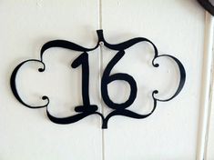 the number sixteen is made out of wrought iron and sits on a white painted wall