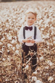 a little boy standing in the middle of a cotton field wearing a bow tie and suspenders