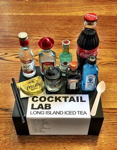 a tray with drinks and condiments sitting on top of a wooden table next to a sign that reads cocktail lab long island iced tea