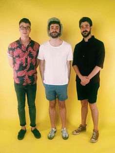 three men standing next to each other in front of a yellow background