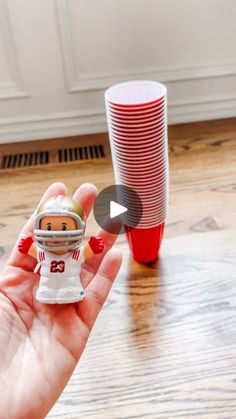 a hand holding a tiny football player figurine in front of a stack of red cups