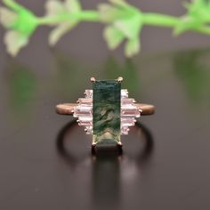 an emerald and diamond ring sitting on top of a black surface with flowers in the background