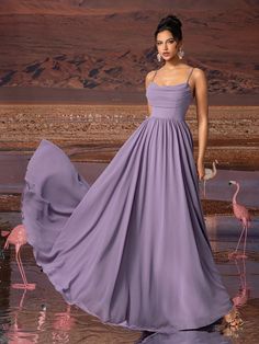 a woman in a long purple dress standing next to flamingos