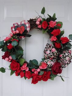 a wreath with red roses and green leaves is hanging on the front door's white door