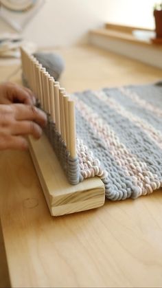 a person is weaving on a wooden table with a crocheted rug in the background