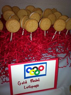 some cookies are sitting on top of red shredded paper and there is a sign that says gold medal lollipops