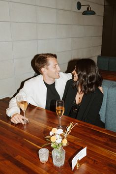 a man and woman sitting at a wooden table with wine glasses in front of them