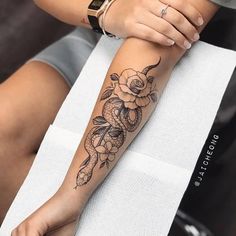 a woman's arm with a rose and snake tattoo on her left forearm, sitting on a towel