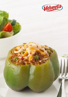 a green pepper stuffed with chili, cheese and other toppings next to a salad