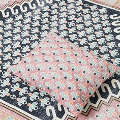 a pink and black rug with an intricate design on the top, next to a pillow