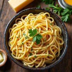 a bowl filled with pasta and parsley on top of a wooden table next to butter