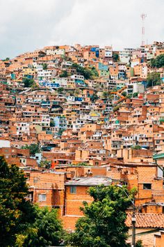 a large group of buildings on top of a hill with trees in the foreground