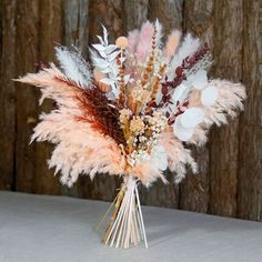 a vase filled with feathers and flowers on top of a white table next to a wooden wall