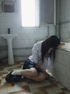 a woman sitting on the floor in a bathroom next to a sink and toilet with her head down