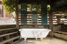 an old fashioned bathtub sits in the middle of a porch with wooden steps and green shutters