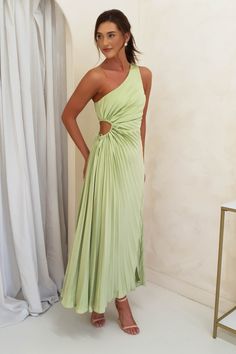 a woman standing in front of a white wall wearing a green dress with one shoulder cut out