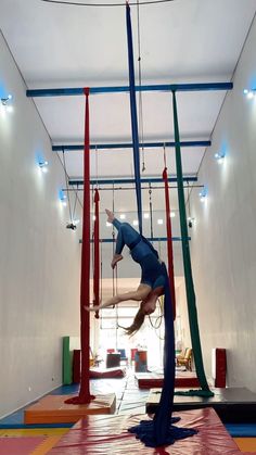 a woman is performing aerial acrobatic tricks in an indoor gym with colorful ropes