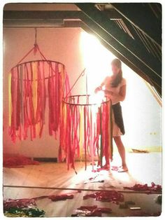 a woman is standing in front of a colorful wind chime with red and yellow streamers hanging from it