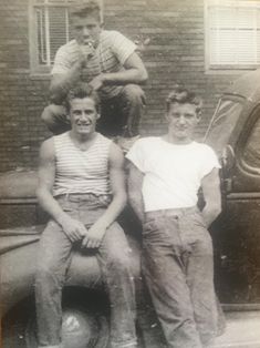 an old black and white photo of three men sitting on the hood of a car