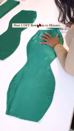 a woman is making a green dress out of satin material on a white counter top