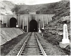 an old black and white photo of train tracks going into a tunnel with mountains in the background