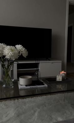 a glass table with flowers and candles on it in front of a flat screen tv