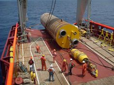 workers are standing on the deck of a ship near a large yellow object in the middle of the ocean