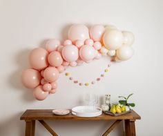 balloons and confetti are arranged on the wall above a wooden table in front of a white wall