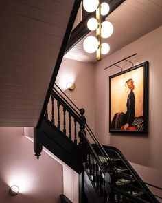 a staircase with a painting on the wall and lights hanging from it's sides