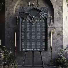 a bat - shaped sign in front of a stone wall with candles and flowers around it