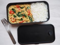 a container filled with rice and vegetables next to a fork on top of a table